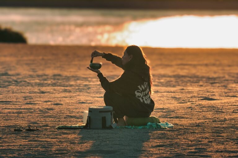 A woman meditates with a sound bowl on a sandy beach at sunrise in Stamford, Connecticut.